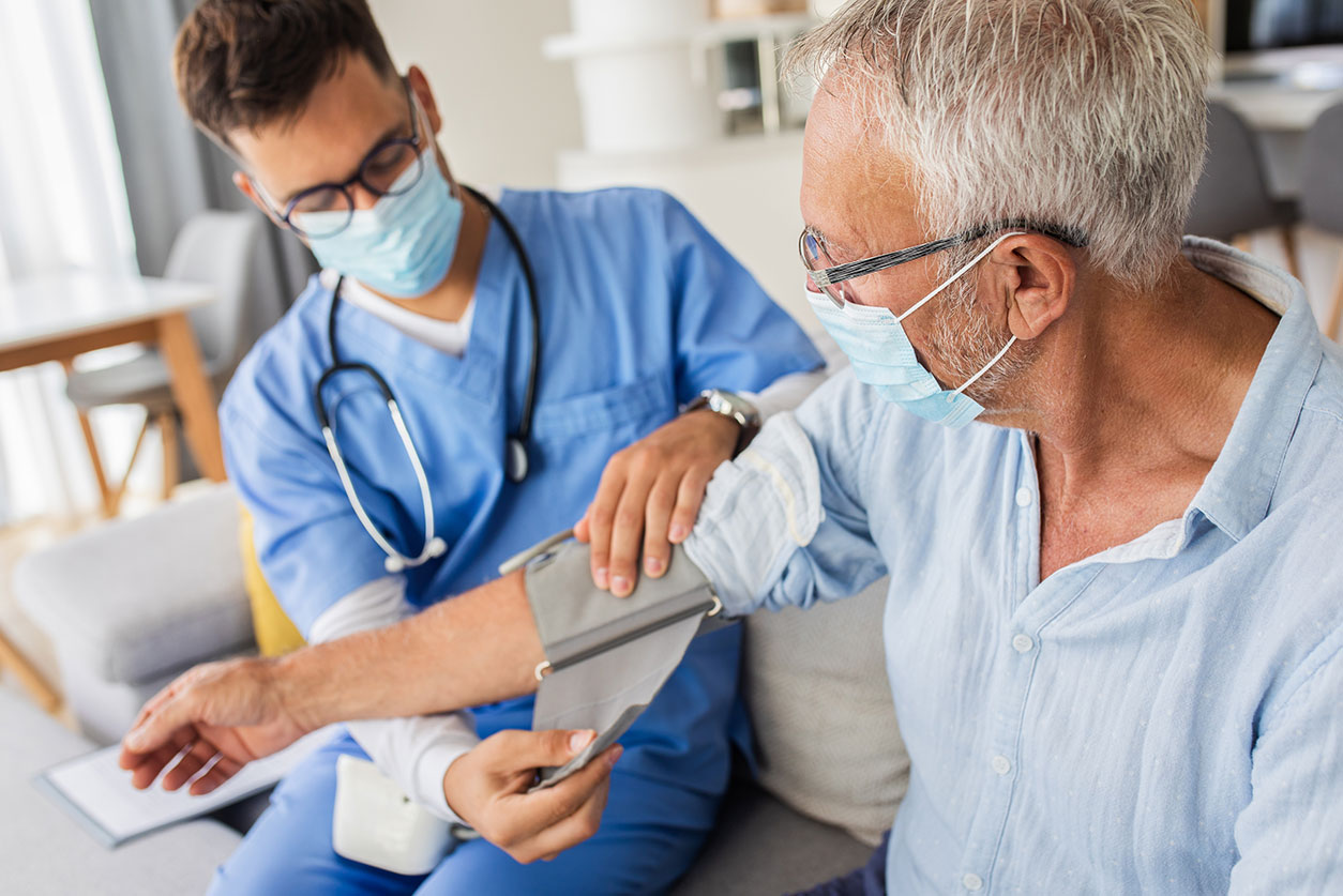 Male nurse measures blood pressure to senior man with mask during visit.
