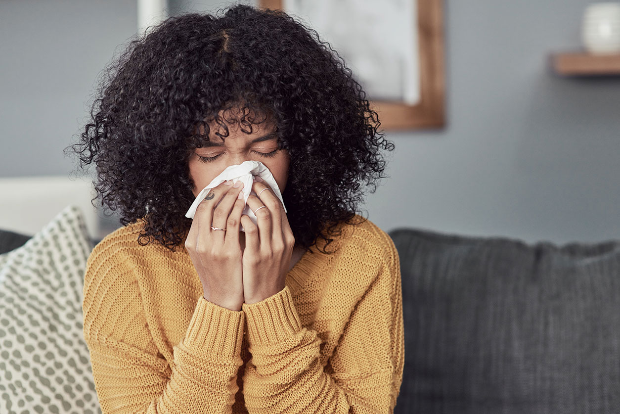 Young woman blowing her nose with a tissue at home - Influenza